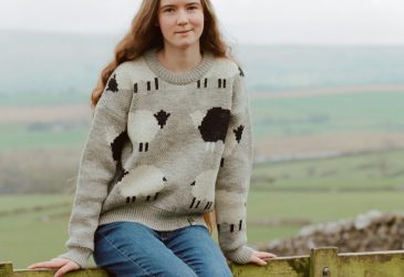 Lady wearing Glencroft British Wool Martha sheep jumper while sitting on fence in Yorkshire Dales