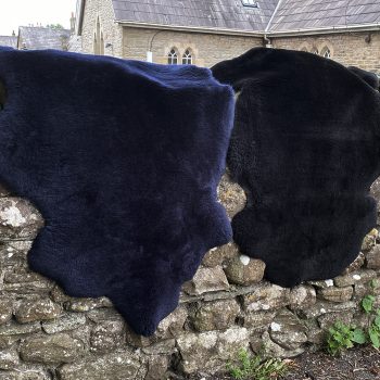 Black and navy short woolled sheepskin rugs draped over a wall