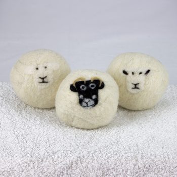 Three felted laundry balls with sheep faces on a fluffy towel
